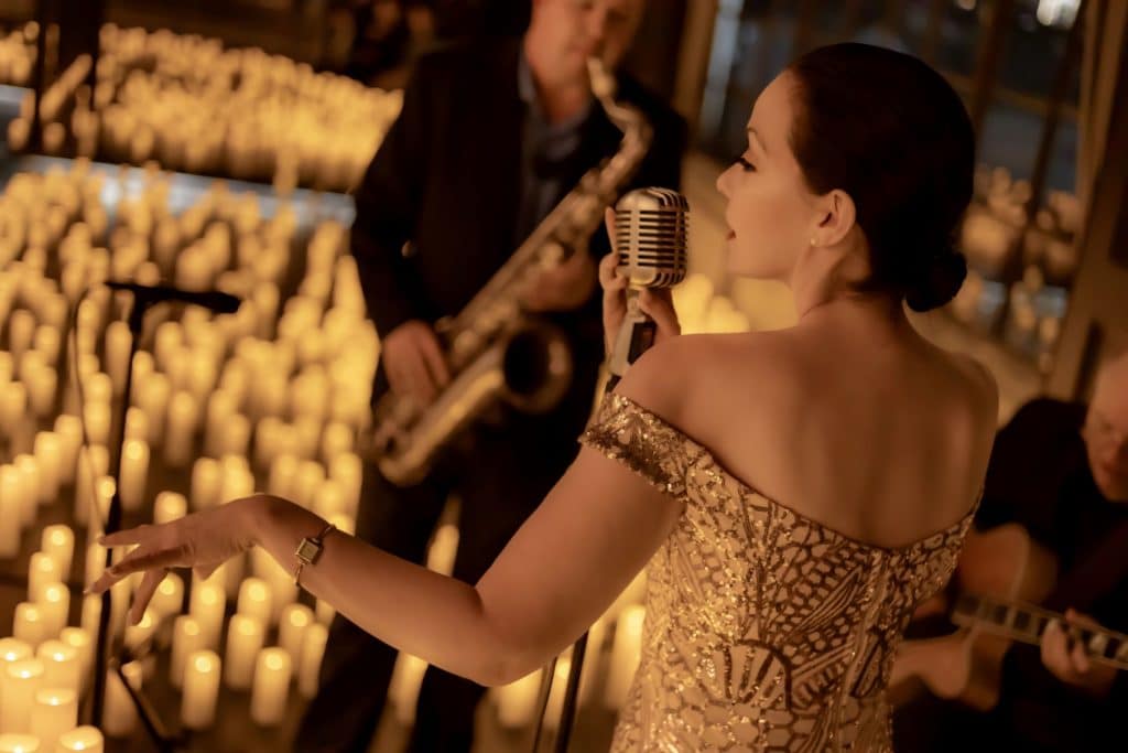 A woman singing on a stage covered in candles with a saxophonist playing beside her.