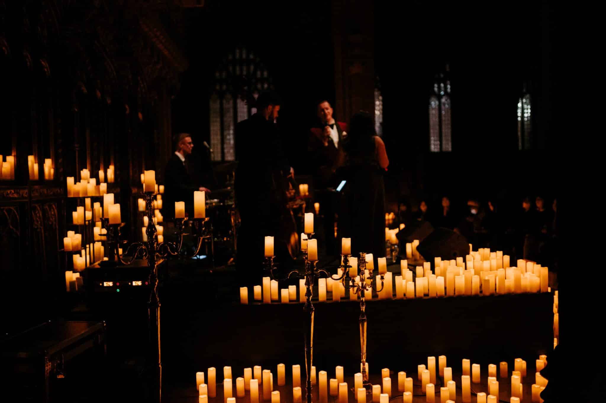 A dark image taken inside Manchester Cathedral showing candles on display and musicians preparing for a performance.