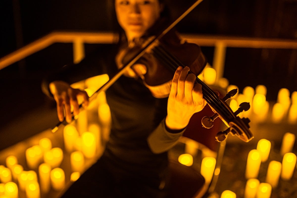 A musician playing the violin with candles in the background