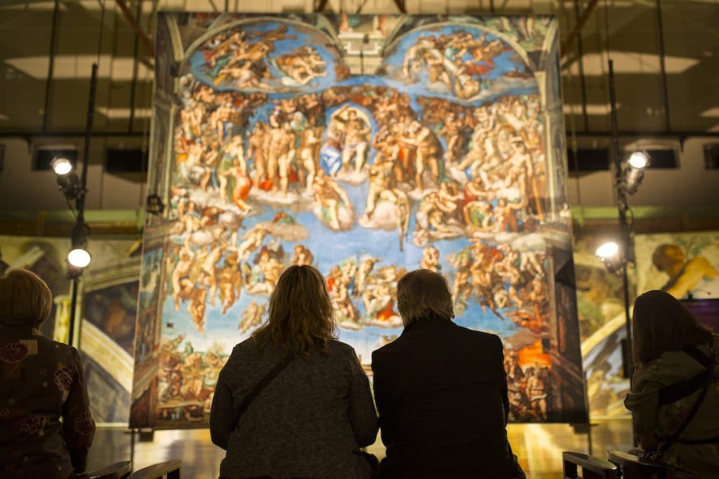 Couple sit silhouetted in front of Last testament section of Sistine Chapel