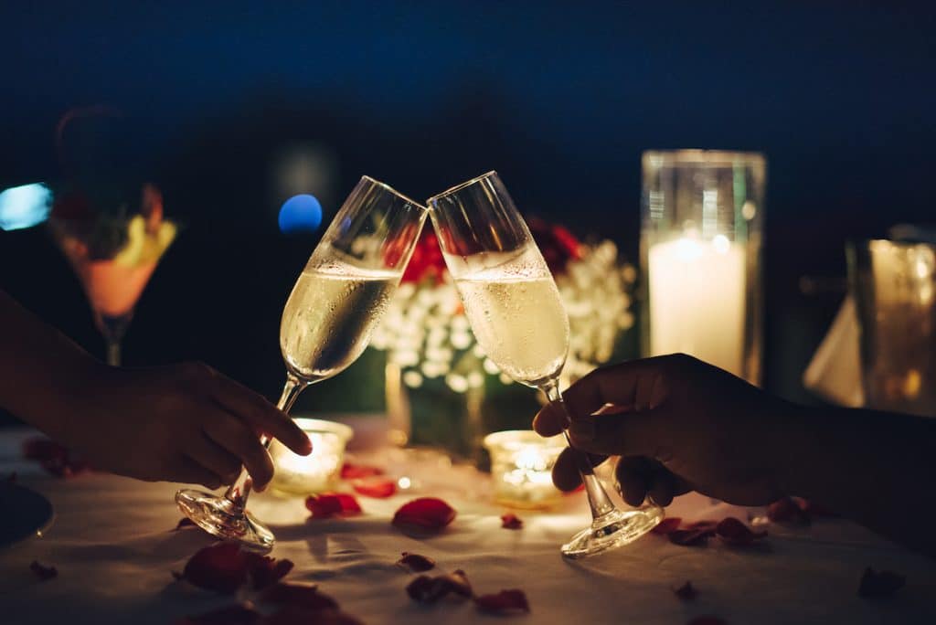 two champagne glasses clinking on table of rose petals