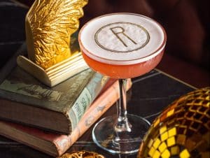rendition-cocktail-in-coupe-glass-next-to-stack-of-books