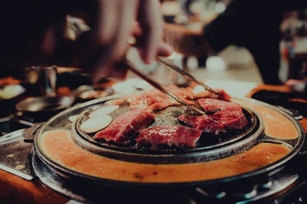 person-turning-meat-with-tongs-on-korean-bbq-grill