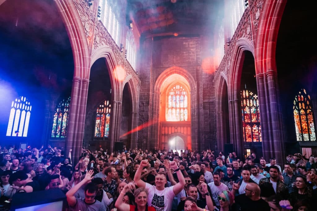 a crowd dances in manchester cathedral with colourful lights
