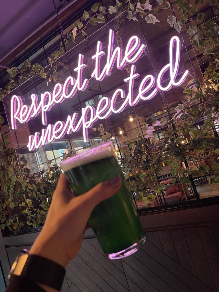 hand-holding-motley-special-green-beer-part-of-st-patricks-day-bottomless-brunch-next-to-neon-sign
