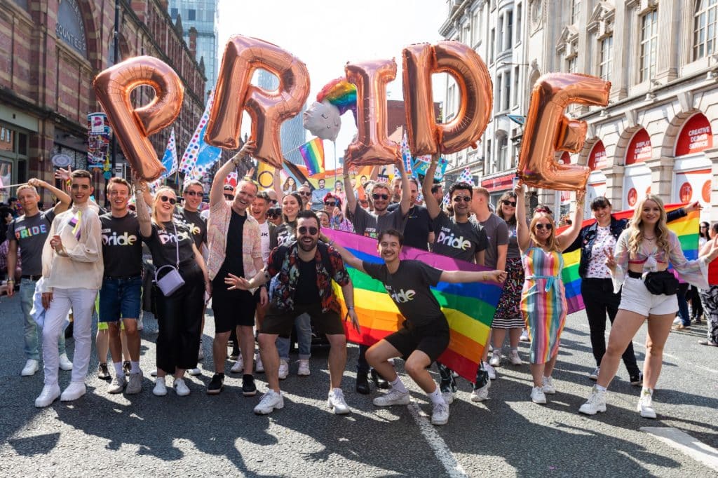 manchester-pride-festival-parade-people-stood-on-deansgate-with-inflatable-balloons-spelling-pride
