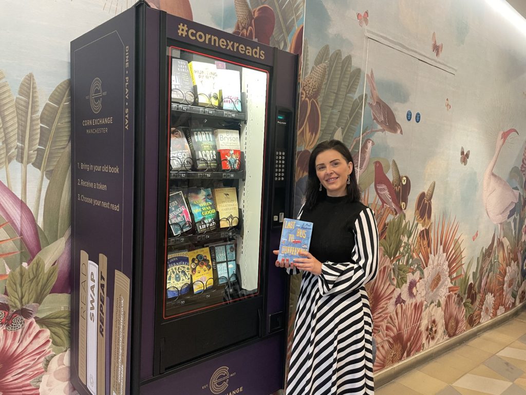 woman-stood-holding-book-next-to-book-vending-machine-in-corn-exchange-manchester
