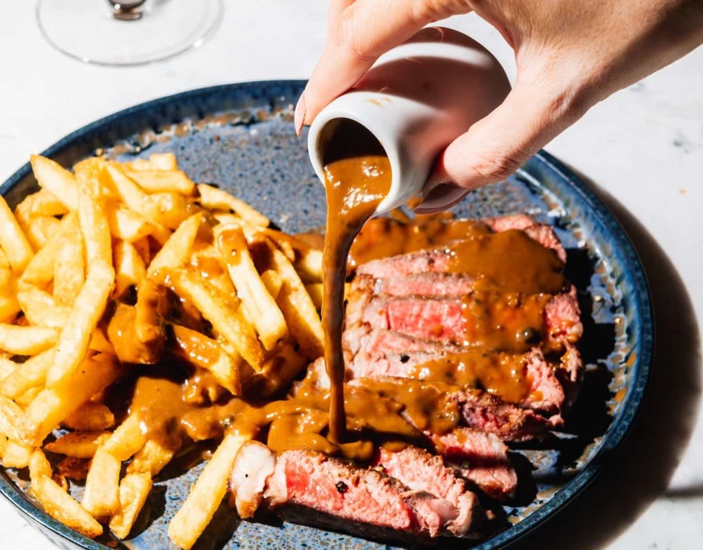 person-pouring-sauce-over-steak-frites-at-garten-bar